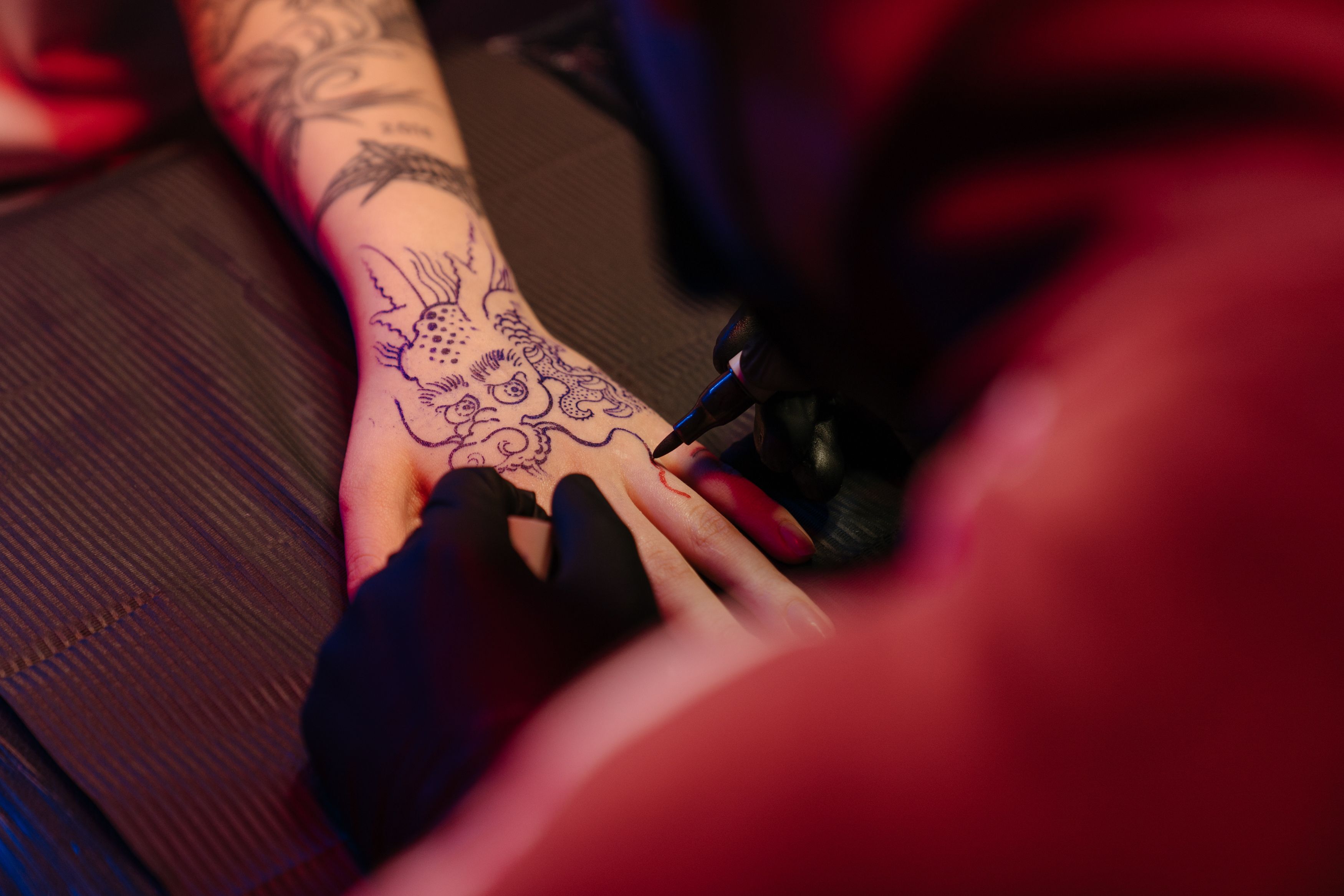 Tatuador em sessão de tatuagem de dragão na mão do cliente